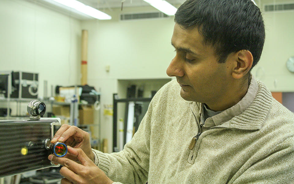 man in a lab adjusting a small metallic ball with a mirror in it attached by a magnet to a large swinging metal arm