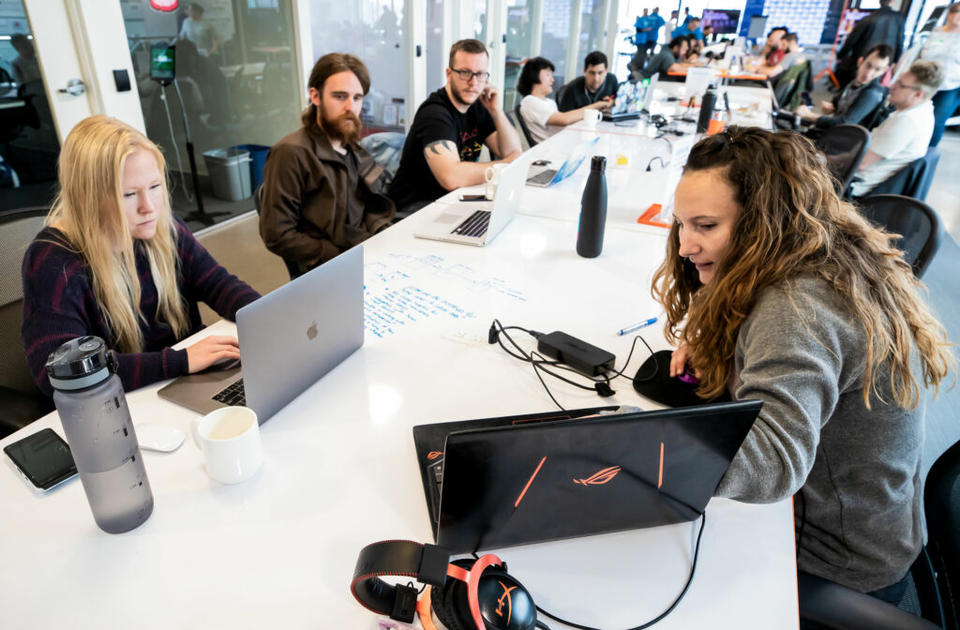 This image shows people sitting around a white table with laptops. In the foreground is two women with laptops.