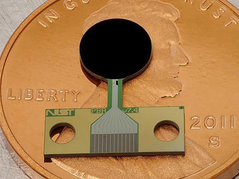 A small flat device with a round black part and a copper-colored rectangular part lies on top of a penny.