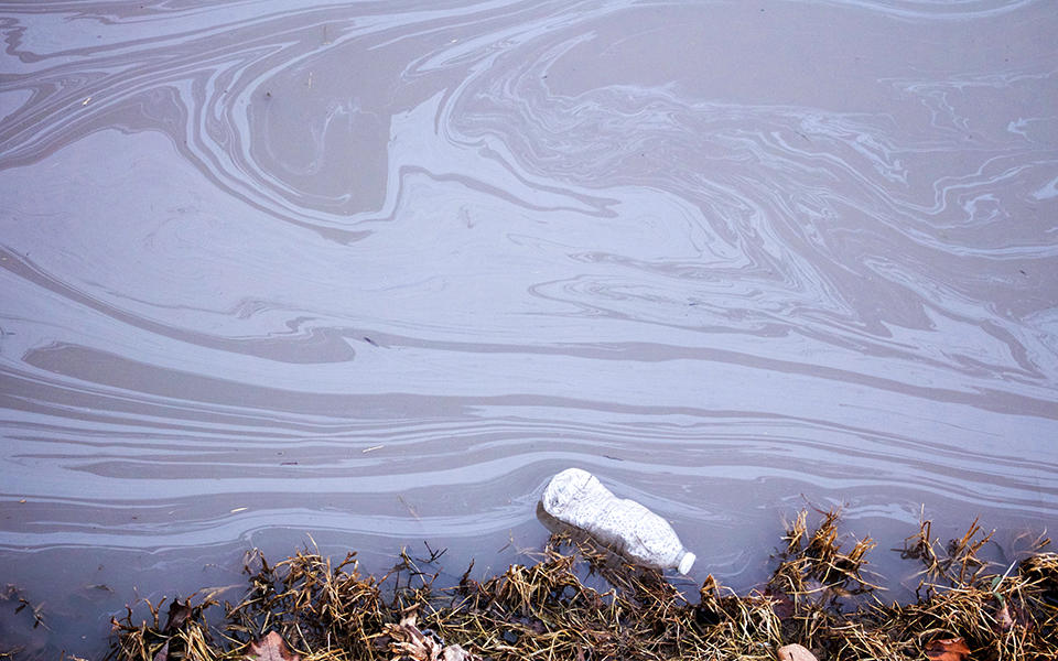 a shoreline with dirty water and bottle floating in it