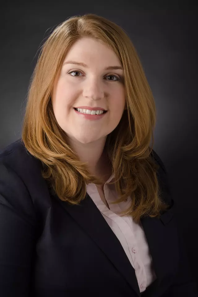 Professional headshot of Sara Orski, a woman with medium length red hair, smiling, wearing a blazer.