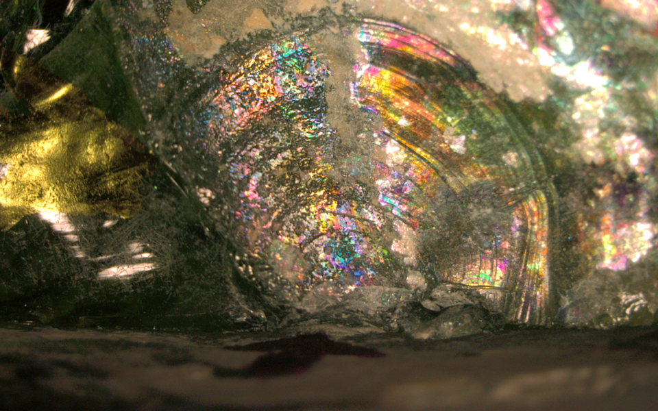 an opalescent close up of Roman glass. There is a clear semi-circular fracture in the center of the piece. 