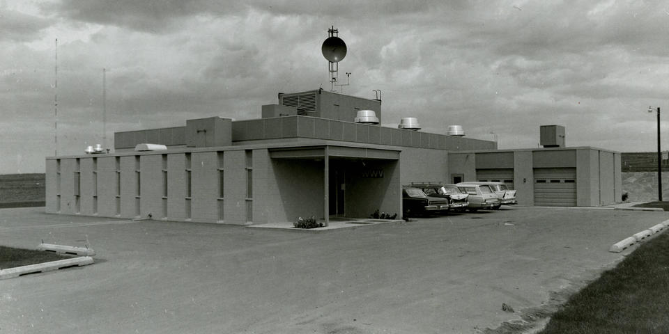 black and white photo of a low building with cars in front.