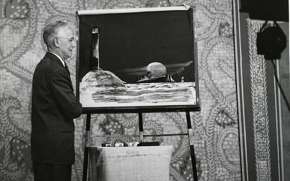 man on a television set in front of a painting of a lighthouse and a ship at sea
