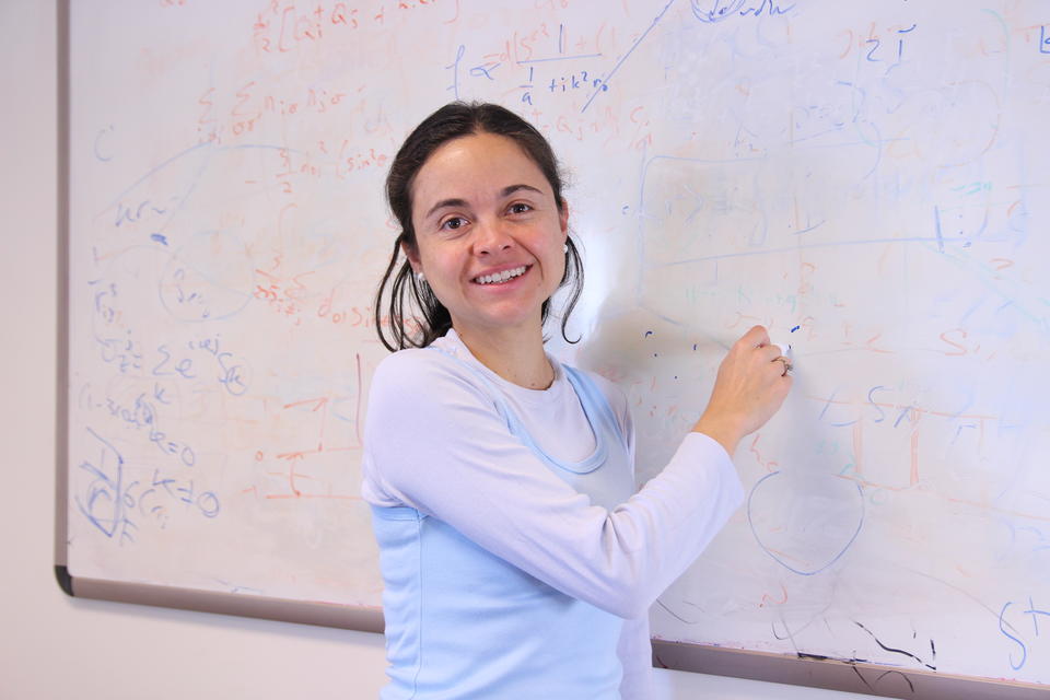 A woman stands at a whiteboard showing scientific formulas.