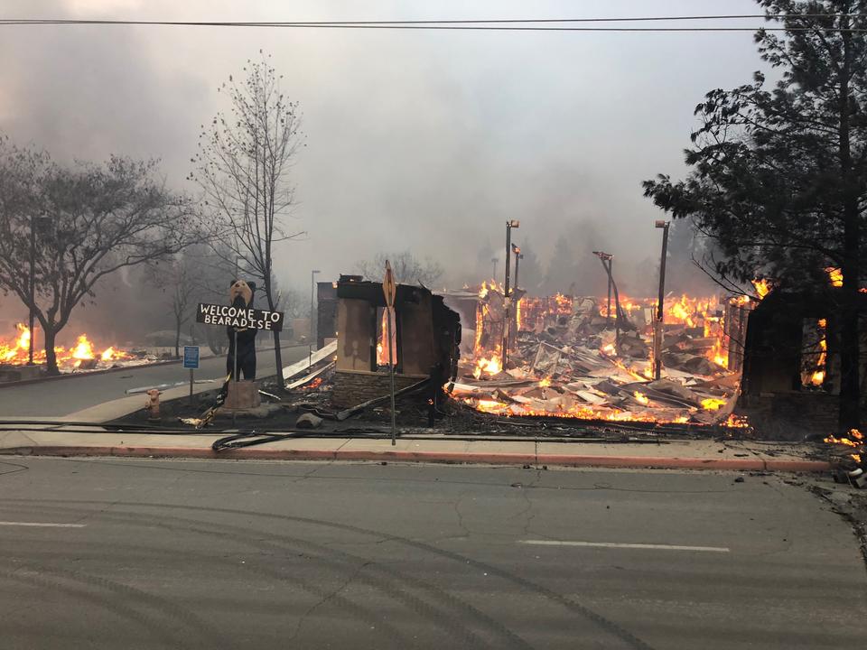 A sign saying "Welcome to Paradise" stands next to a burning building.