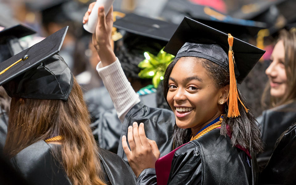 A female student at Howard Community College Commencement turning behind in her seat and smiling while holding up her diploma.