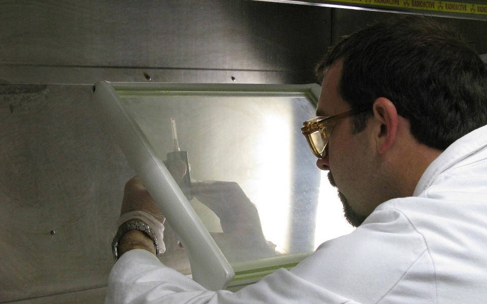 Denis Bergeron working behind an L-shield with a syringe containing a radiopharmaceutical.