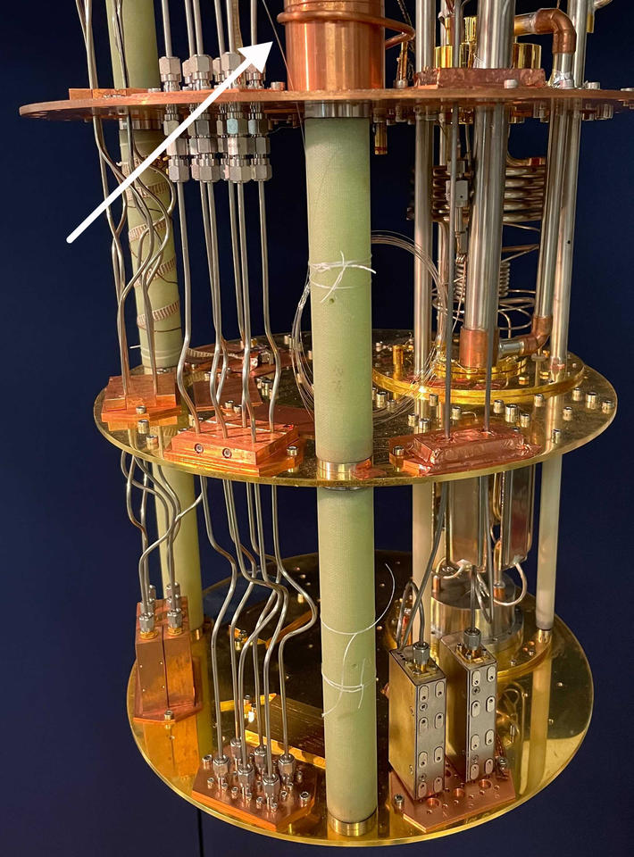 White arrow points to tiny fiber running vertically through large metal device (cryostat)