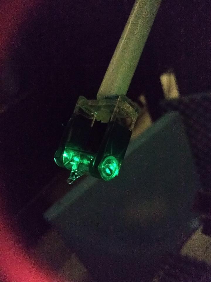 Tiny glass vial in holding device glows green in dark photo.