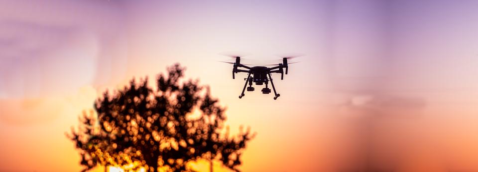 A drone flies against the setting sun.