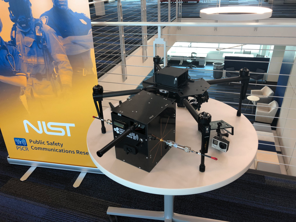 Stabilized drone on table with LTE deployable. Sign in the background reads NIST Public Safety Communications Research.