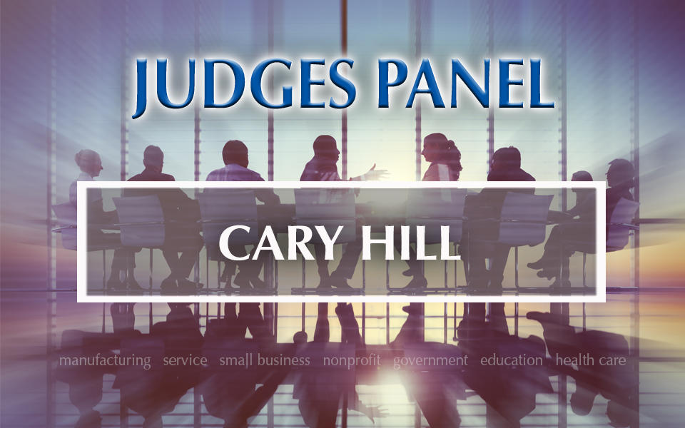 Baldrige Judges Panel Cary Hill with a background panel of people having a discussion.