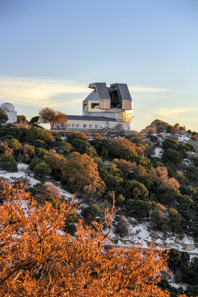 A blocky telescope structure sits on top of a wooded hill with autumn colors.