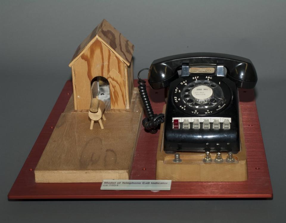 An old-fashioned phone with lights attached is displayed next to a wooden toy with a barn and animal. 