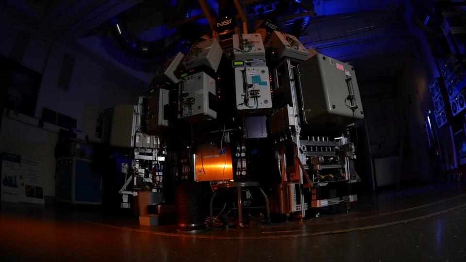 Large scientific instrument with metal boxes around the outside fills a darkened room. 