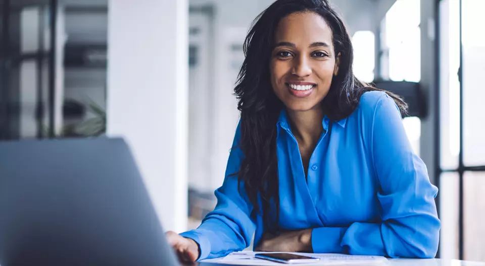 Woman sitting at a table while leaning on her hand and using her laptop to apply to become a Baldrige examiner.