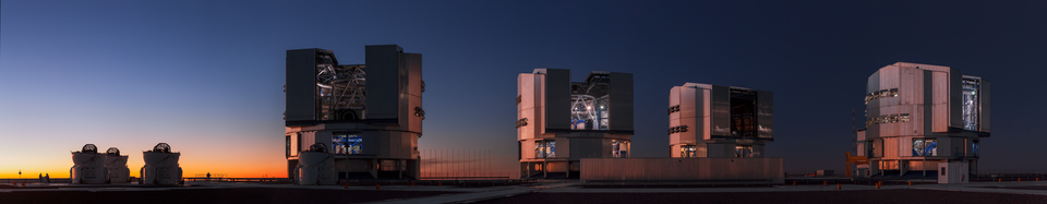 Several large telescope structures stand in the desert against a darkened sky.