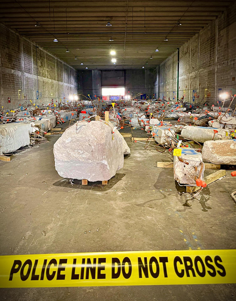 Large chunks of concrete bristling with rebar and colored flags sit in a warehouse. 
