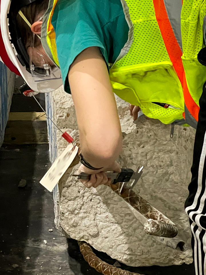 A researcher in safety gear bends over a large piece of concrete and rebar, performing tests with a handheld tool.