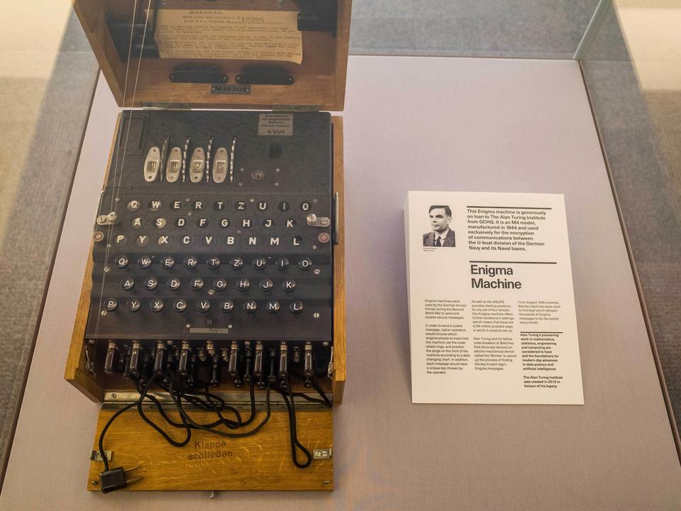 Left: Machine that looks like an old fashioned typewriter in a box. Right: picture of Alan Turing along with a bio. Both are from a museum exhibit.