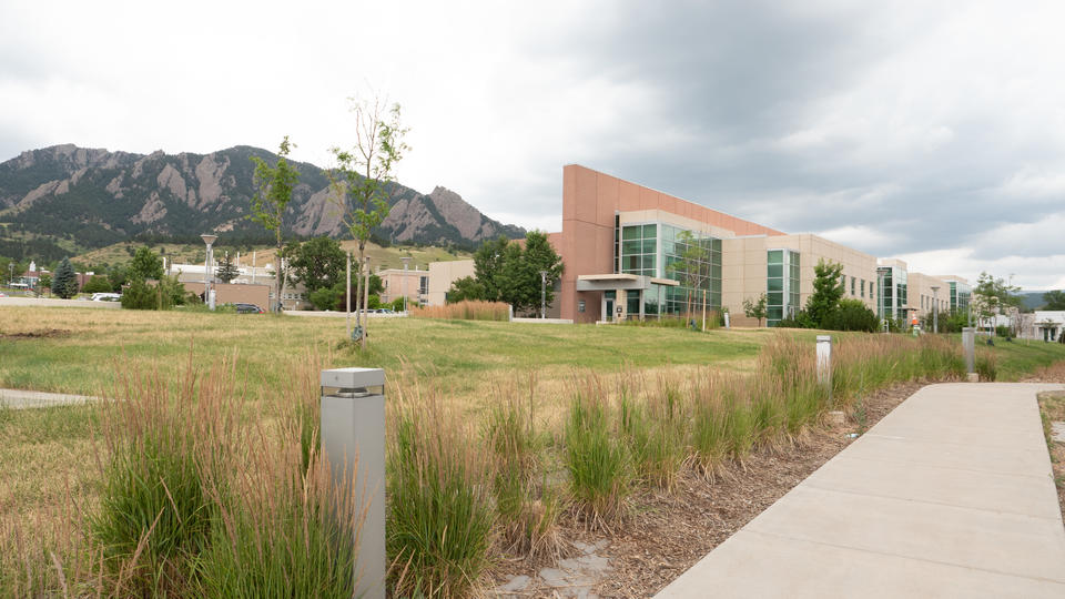 Sidewalk in foreground, with an angular office building to the right and mountains and a cloudy sky in the background.