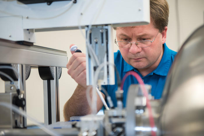 Alexander Grishaev leans over a counter full of scientific equipment, looking down at his work. 