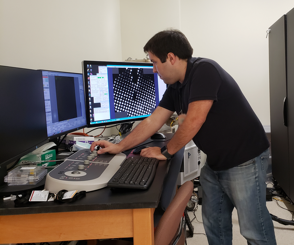 Thomas Cleveland stands at a desk, looking at a computer screen while turning a dial on a control panel. 