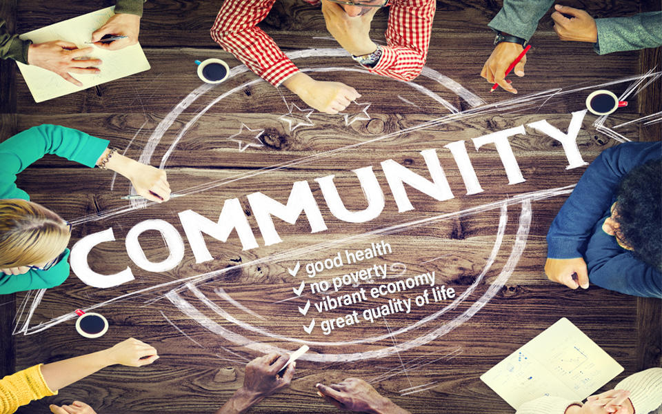 Group of people looking at text on a table that says Community - good health, no poverty, vibrant economy, great quality of life.