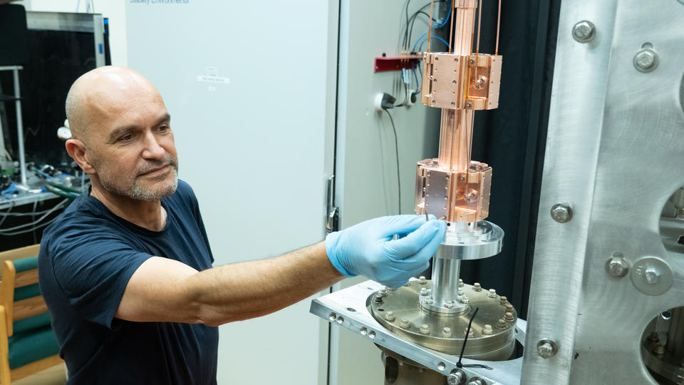 A man wearing latex gloves reaches out to adjust something on a cylindrical metal scientific device.