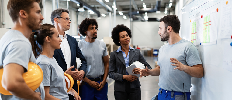 Young worker giving presentation in front of whiteboard in a factory. 