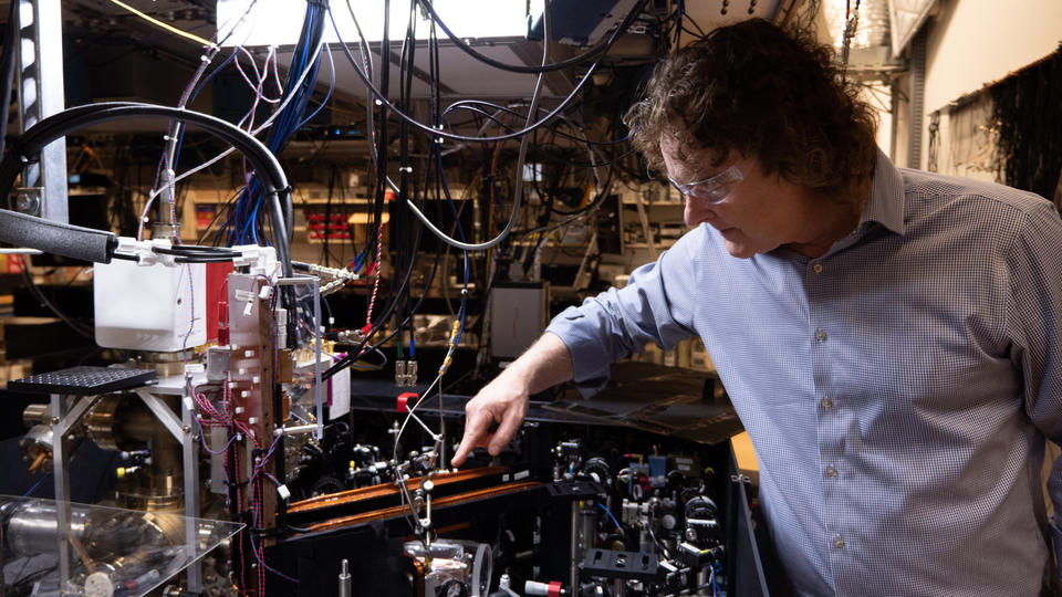 Andrew Wilson leans over a table packed with small devices in the lab. Loops of wire hang overhead and connect to other equipment. 