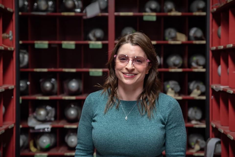 A woman in safety glasses stands between rows of metal cylinders.