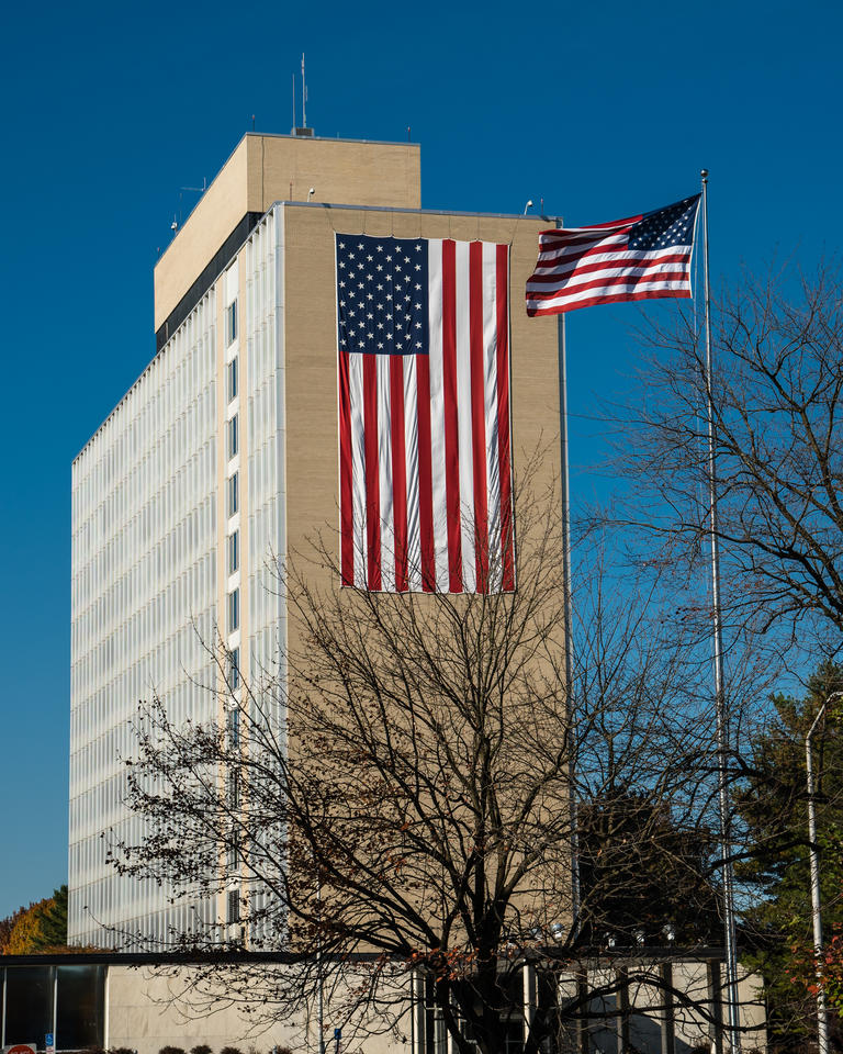 11 story building with an American flag draped down the side of the building and also an American flag on a pole.