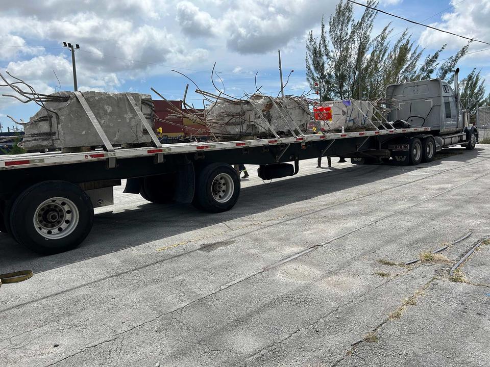 A long trailer parked outdoors holds pieces of concrete with broken metal bar around the edges.