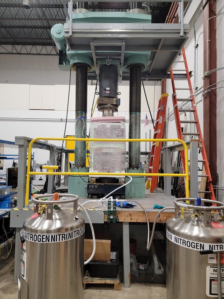 A large hydraulic press machine with vertical columns stands on a platform behind tanks labeled "Nitrogen."