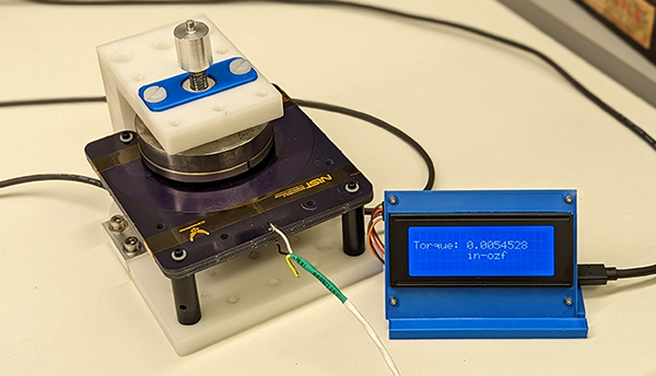 Tabletop scientific device includes circular magnets mounted on a black platform wired to a small screen with a torque readout.