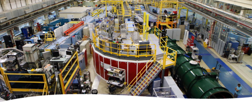 Interior view of a long, multistory scientific facility filled with large tubular guides, elevated walkways, and electronic instrumentation.