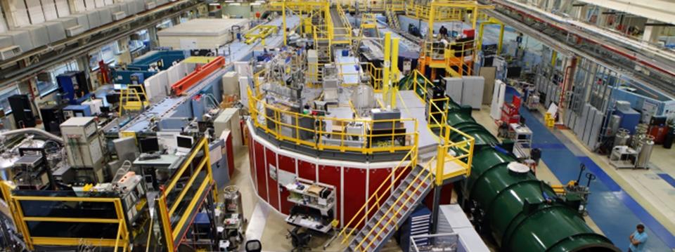  Interior view of a long, multistory scientific facility filled with large tubular guides, elevated walkways, and electronic instrumentation.