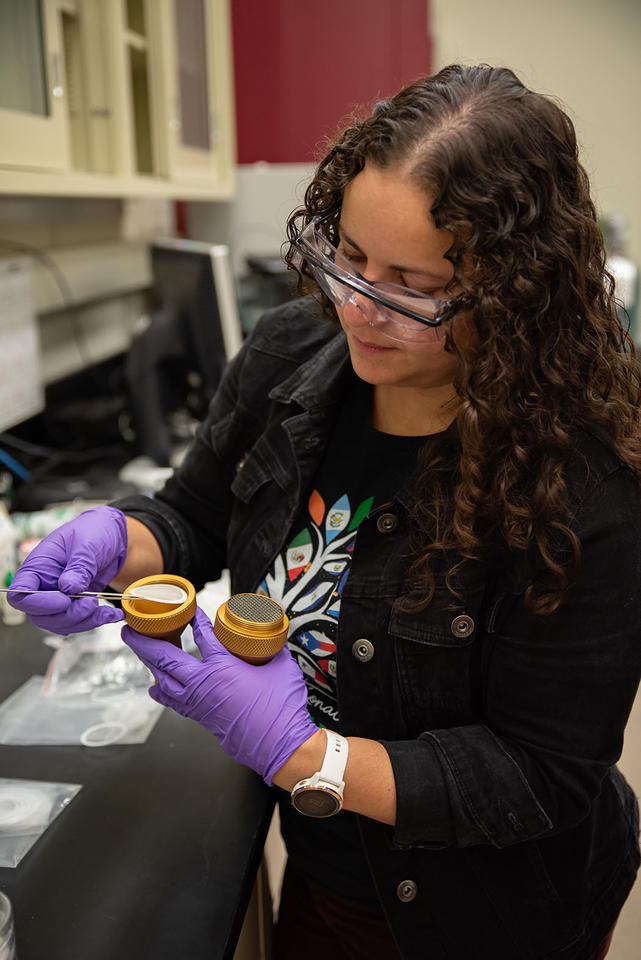 Diana Ortiz-Montalvo uses tweezers to place a filter into a small holder in the lab. 