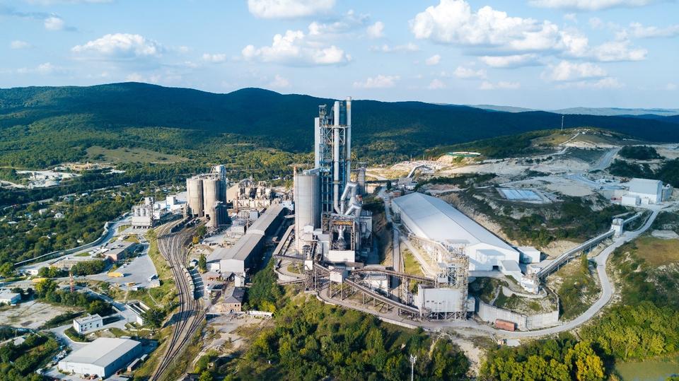 Ariel photography of a cement manufacturing facility showing buildings, roads, towers, stacks, and storage. 