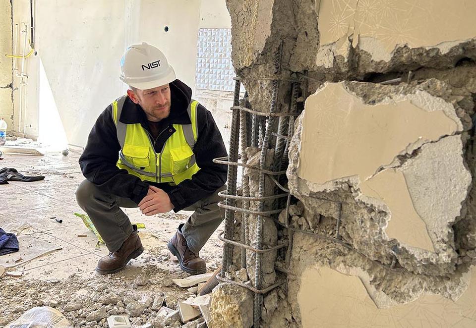 A man in safety gear crouches to examine a damaged wall inside a building after an earthquake. 
