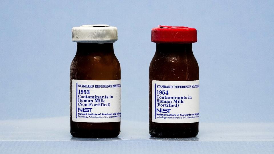 Photograph showing two amber vials against a light blue background, with silver and red colored caps and labels that identify the contents.