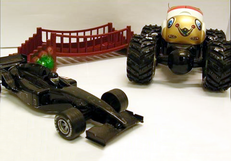 Photograph of a toy race car, toy monster truck with snail face, and sagging toy bridge. 