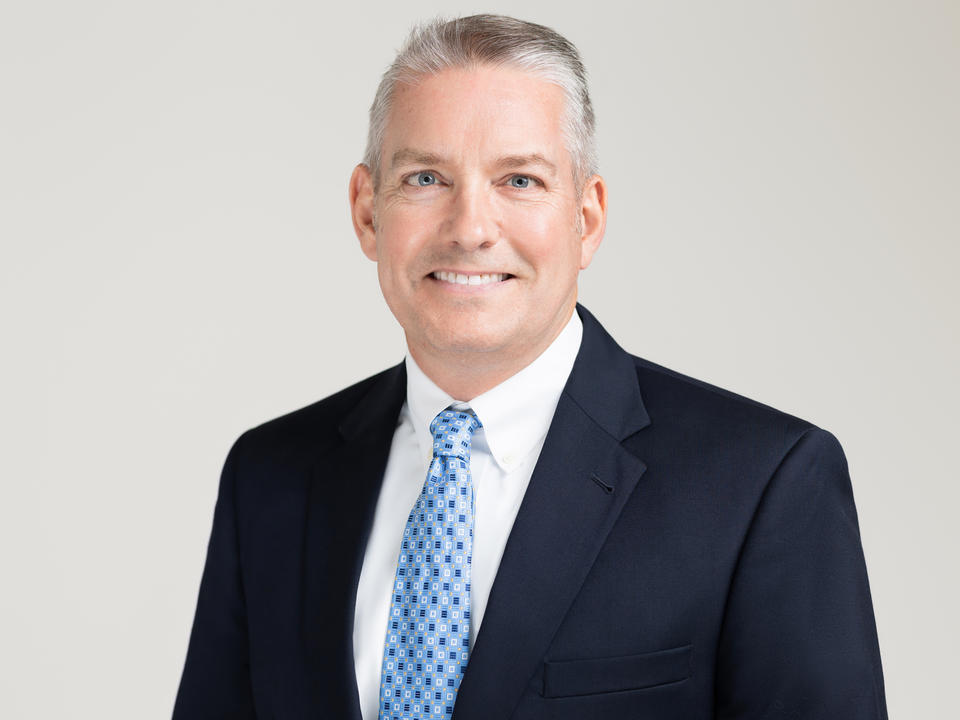 headshot of a man with gray hair in a suit. white shirt. blue tie. black jacket