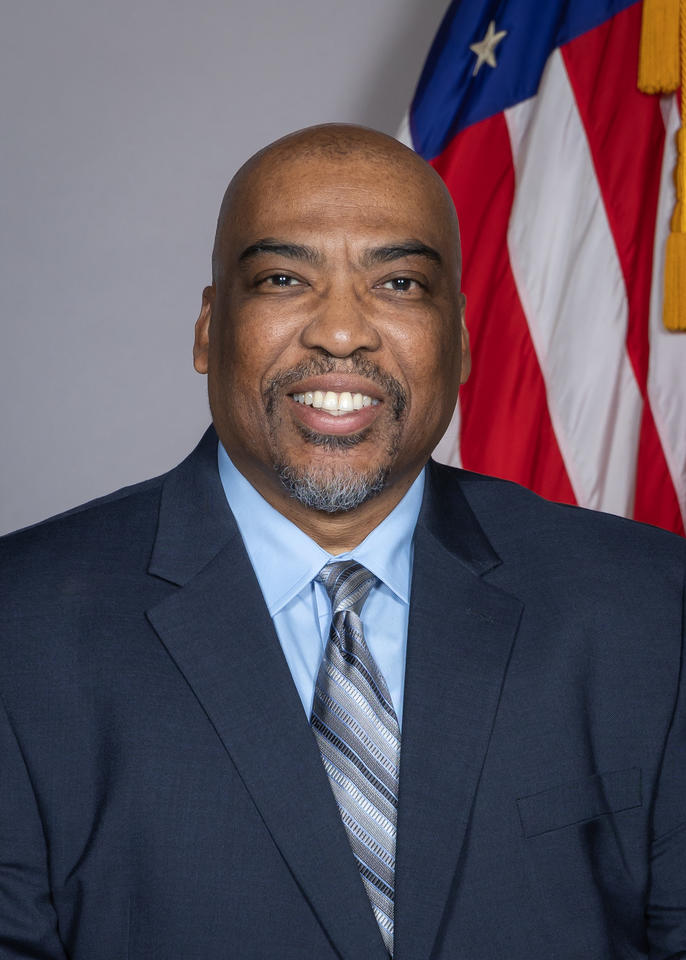 Essex Brown poses for a head shot with an American flag in the background.