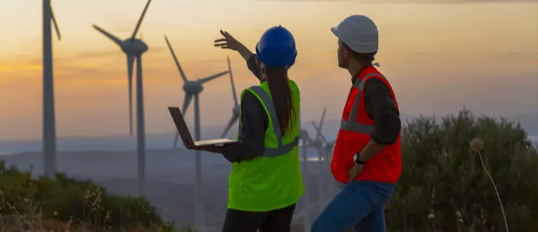 Young maintenance engineer team working in wind turbine farm at sunset