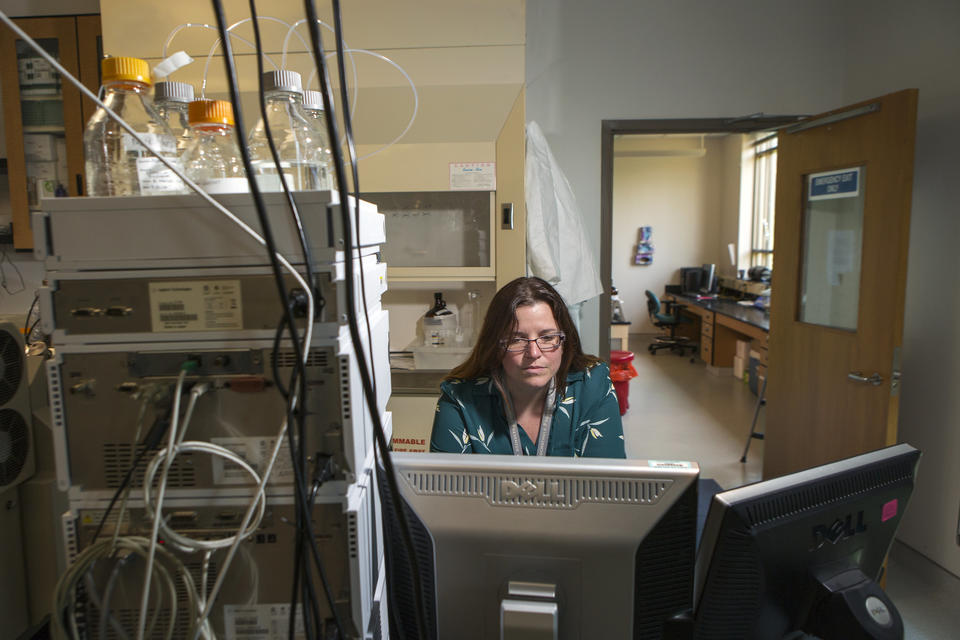 Photograph of a woman studying a computer monitor, seated in a laboratory.