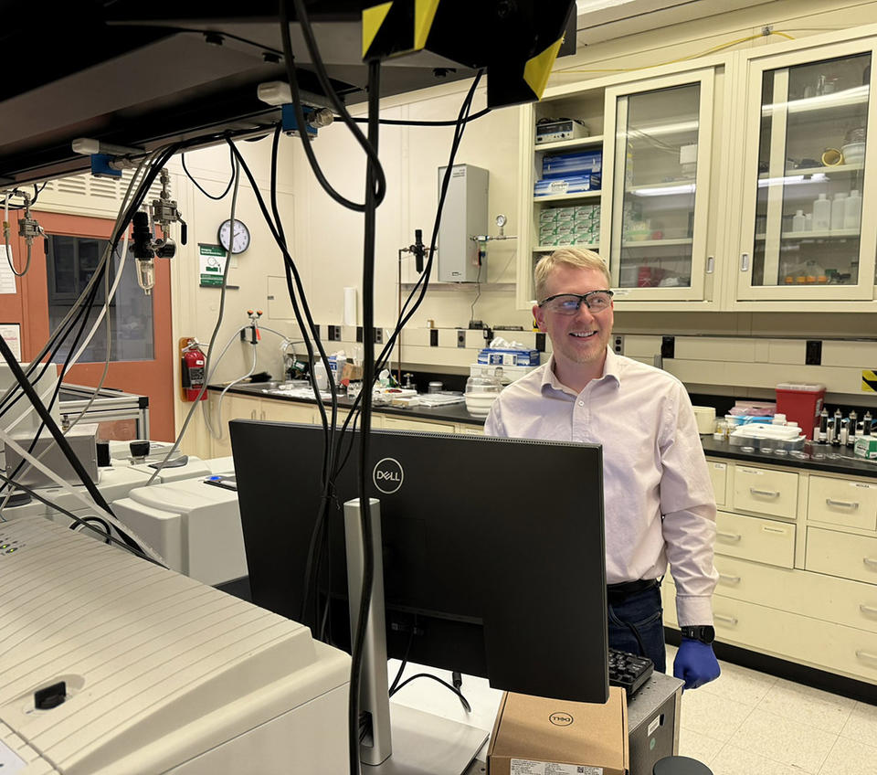 Brad Sutliff wears safety glasses as he stands in the lab in front of a computer monitor.