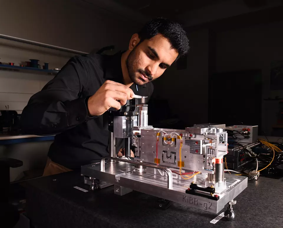 A person in a black shirt works on a mechanical device in a lab setting.